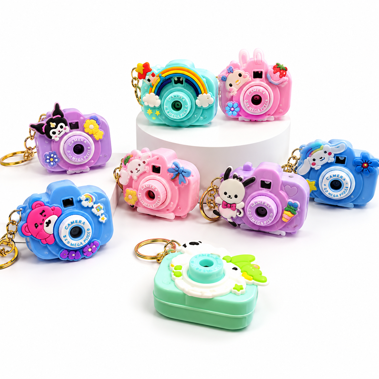 A set of colorful camera-shaped keychain charms and a matching camera-shaped case, shown on a clean white background. The charms come in multiple pastel colors including pink, blue, purple, teal, and mint green, each decorated with cute cartoon animal faces, flowers, stars, and small accessories.