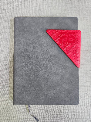 Gray leather-bound book with a red triangular bookmark on a textured gray surface