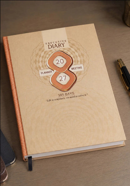 A beige leather-bound executive diary with a textured cover, featuring a central metallic rose-gold and white emblem that reads '20 MEETING 27 365 DAYS'. The diary is shown on a wooden desk next to a black pen.